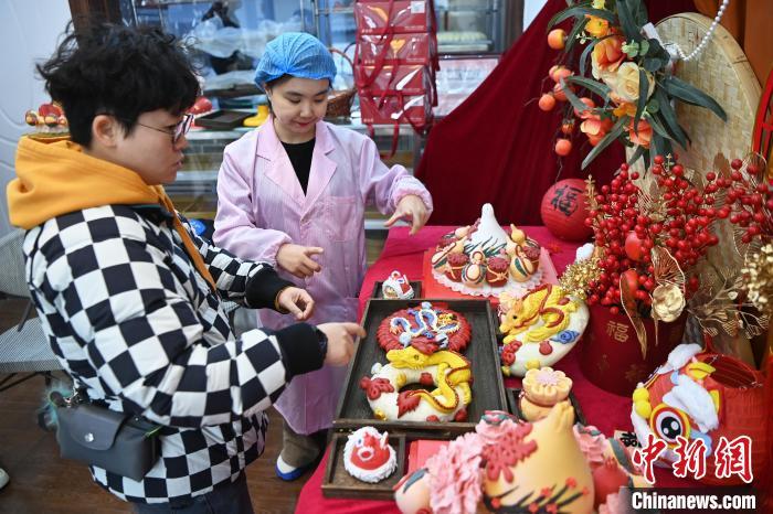 1月25日，隨著春節(jié)臨近，蘭州一花饃店“龍”元素花饃熱銷。圖為工作人員向顧客推薦“龍”元素花饃。九美旦增 攝</p><p>
